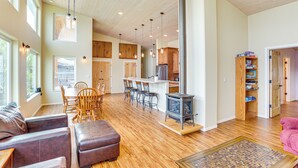 A spacious living area with a wooden floor, a large fireplace, and a dining area with wooden chairs and a table. - Lake Whatcom House w/ Private Hot Tub + Dock (Bellingham)