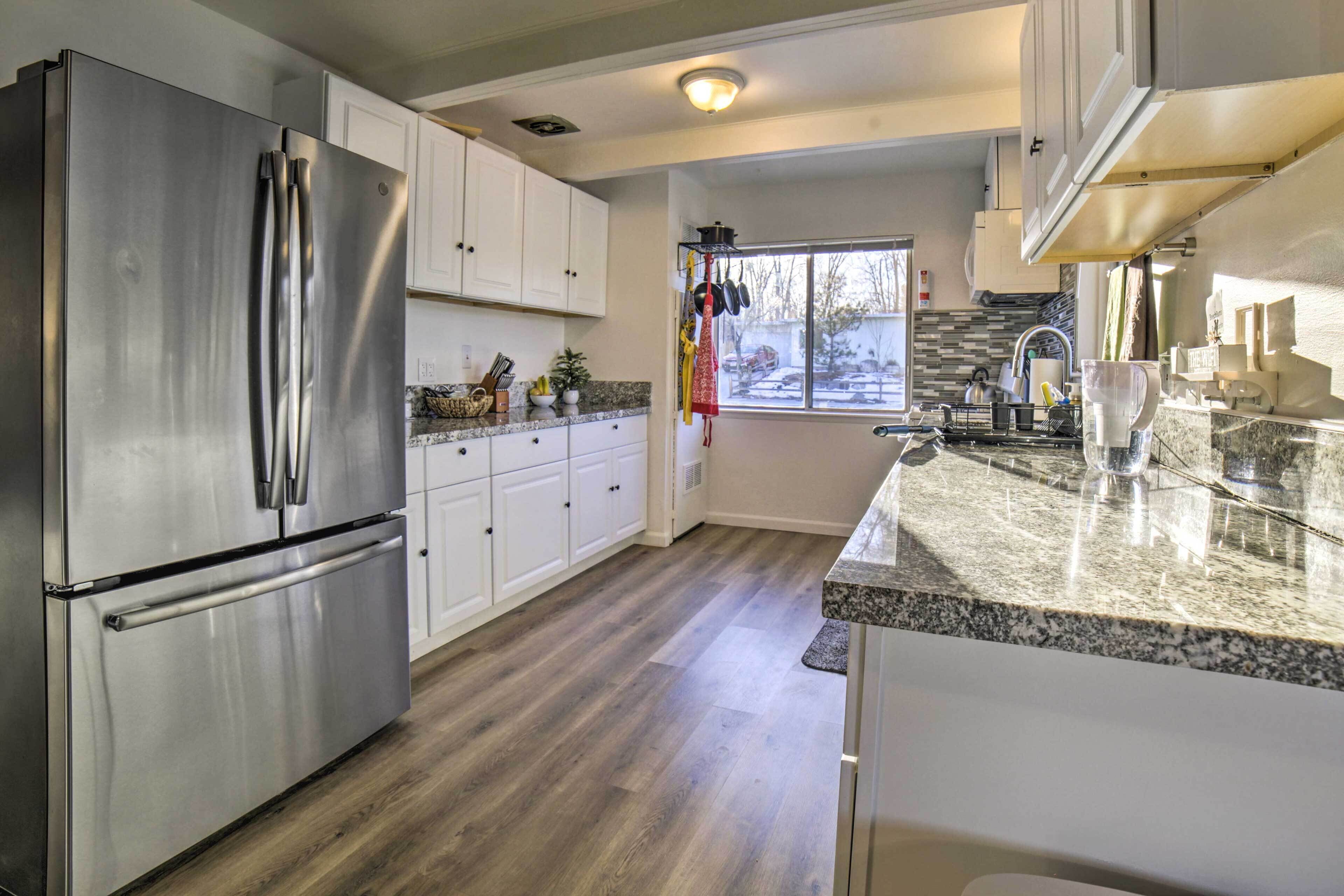 A modern kitchen with stainless steel appliances, white cabinets, granite countertops, and a large window providing a view of the outdoors.