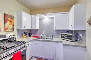 A kitchen with white cabinets, a gas stove, a microwave, and a red cutting board.