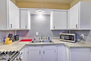 A kitchen with white cabinets, a double sink, a gas stove, a microwave, and a red cutting board.