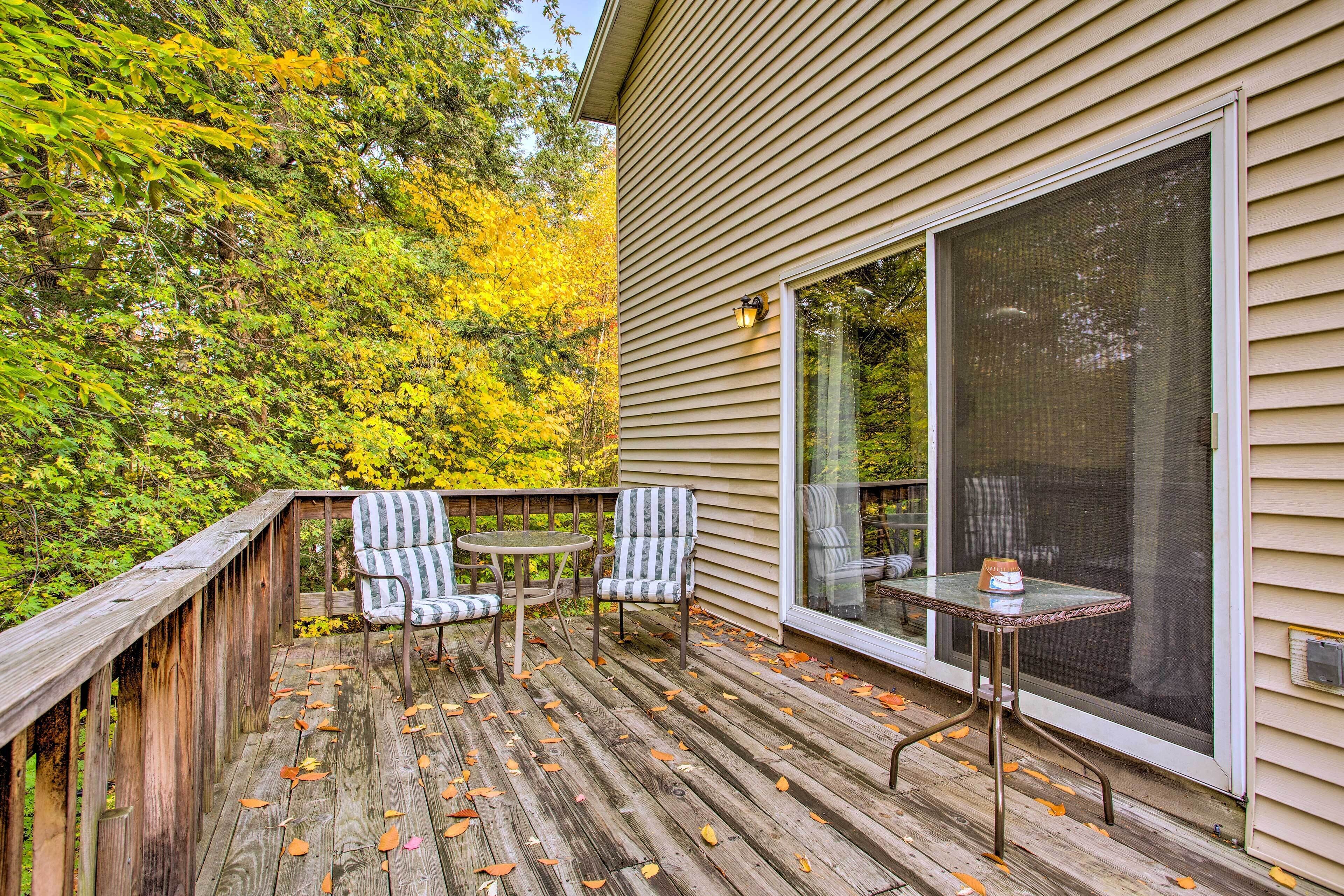 A wooden deck with two chairs and a table, overlooking a forested area.