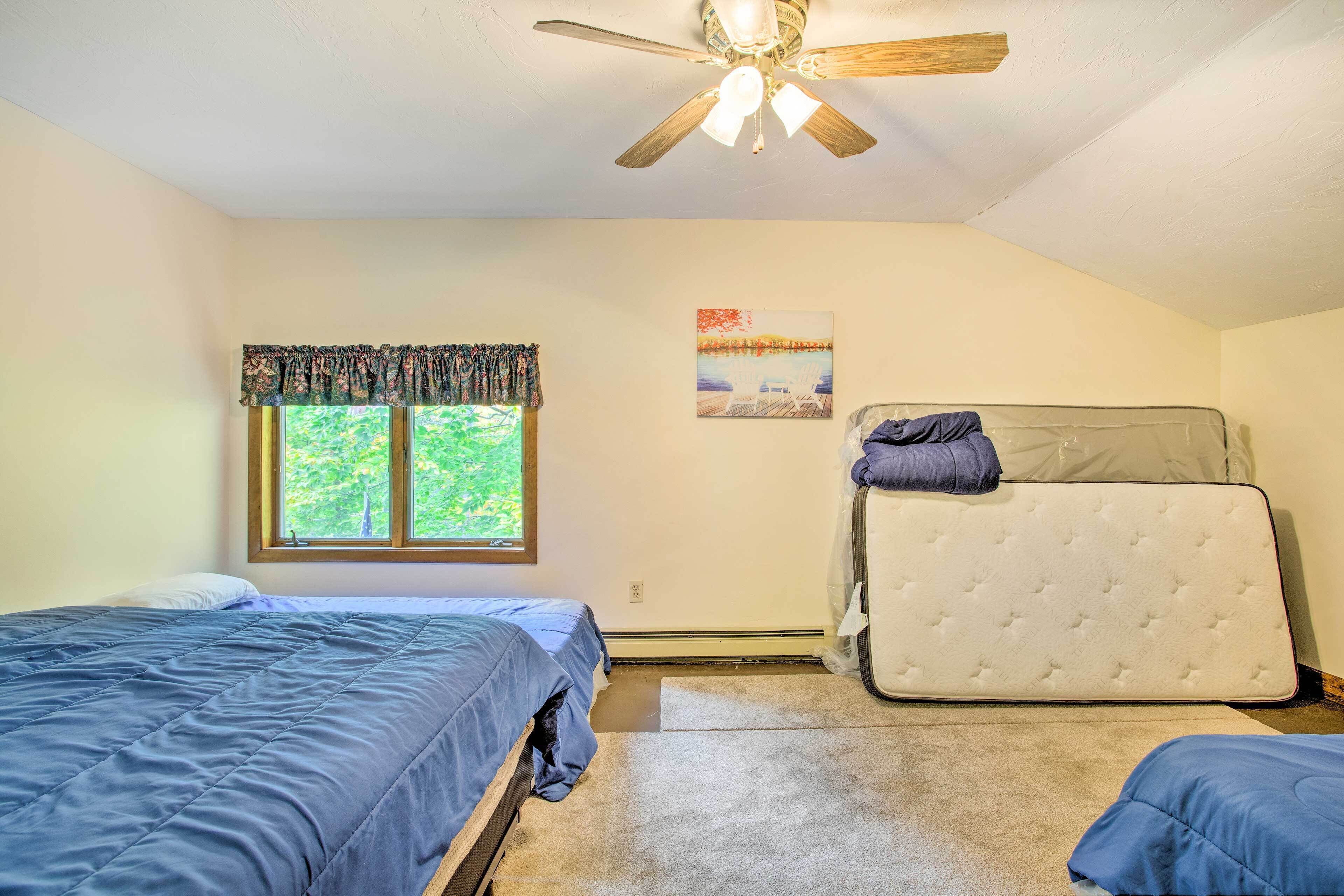 A bedroom with two beds, a ceiling fan, a window with curtains, and a painting on the wall.