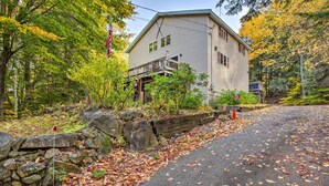 A two-story house with a porch, surrounded by trees and a stone wall.