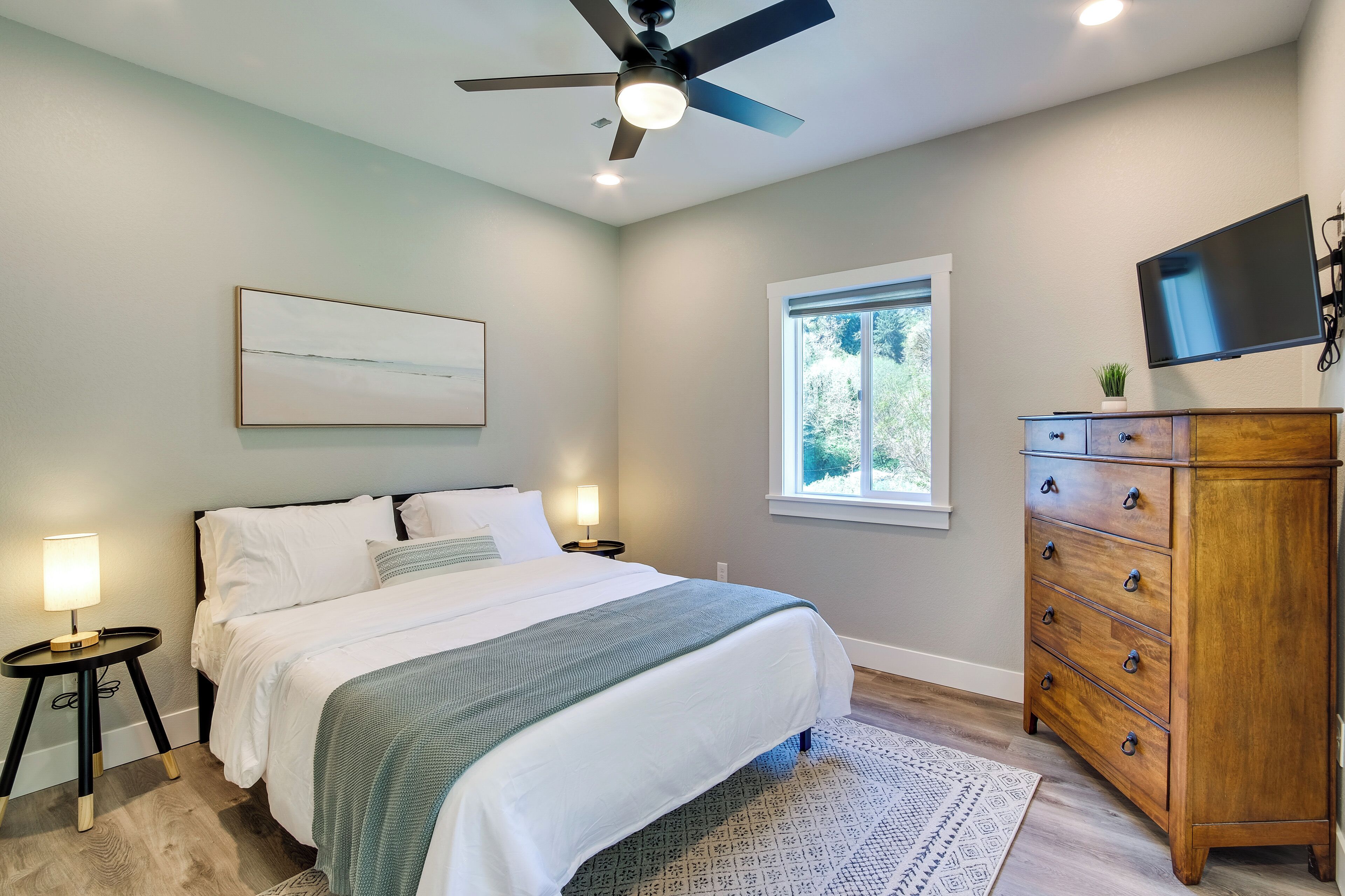 Une chambre à coucher comprenant un lit, des tables de chevet, une commode, un ventilateur de plafond, un téléviseur et une fenêtre.