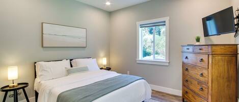 Une chambre à coucher comprenant un lit, des tables de chevet, une commode, un ventilateur de plafond, un téléviseur et une fenêtre.