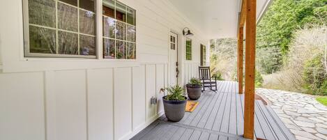 A covered porch with a wooden deck, white exterior walls, and large windows.