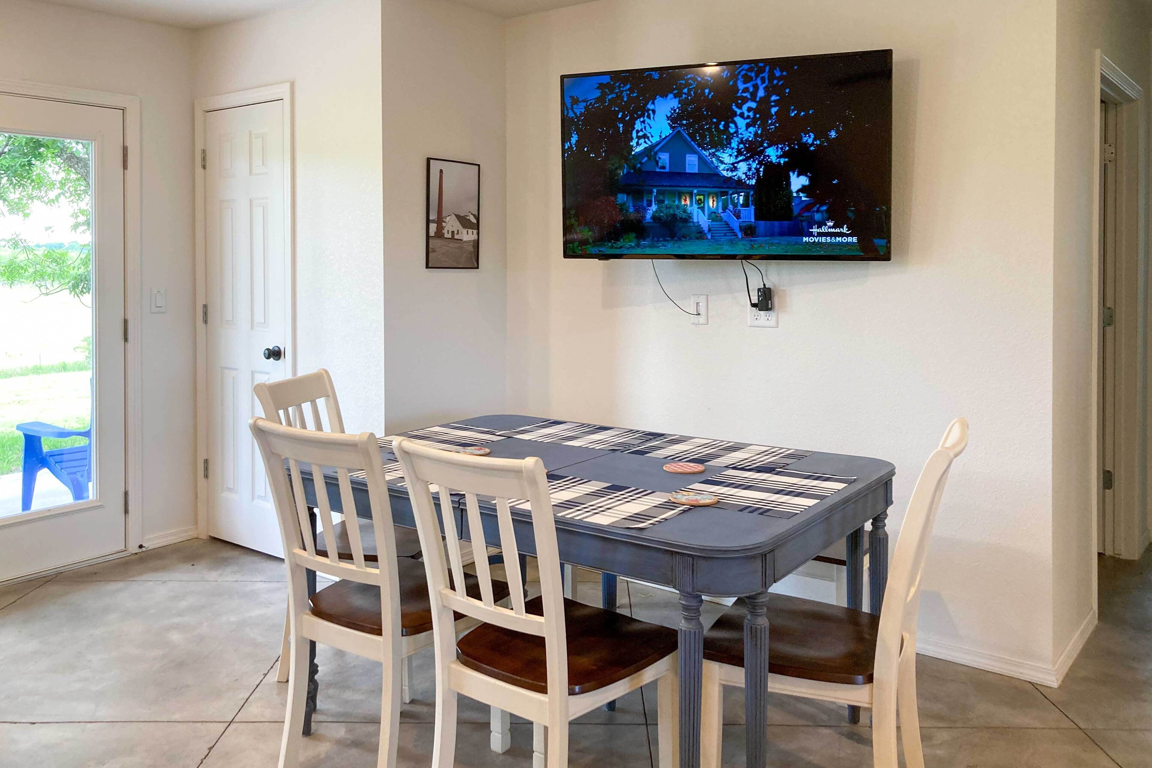 A dining area with a table set for four, a television mounted on the wall, and a door leading outside.