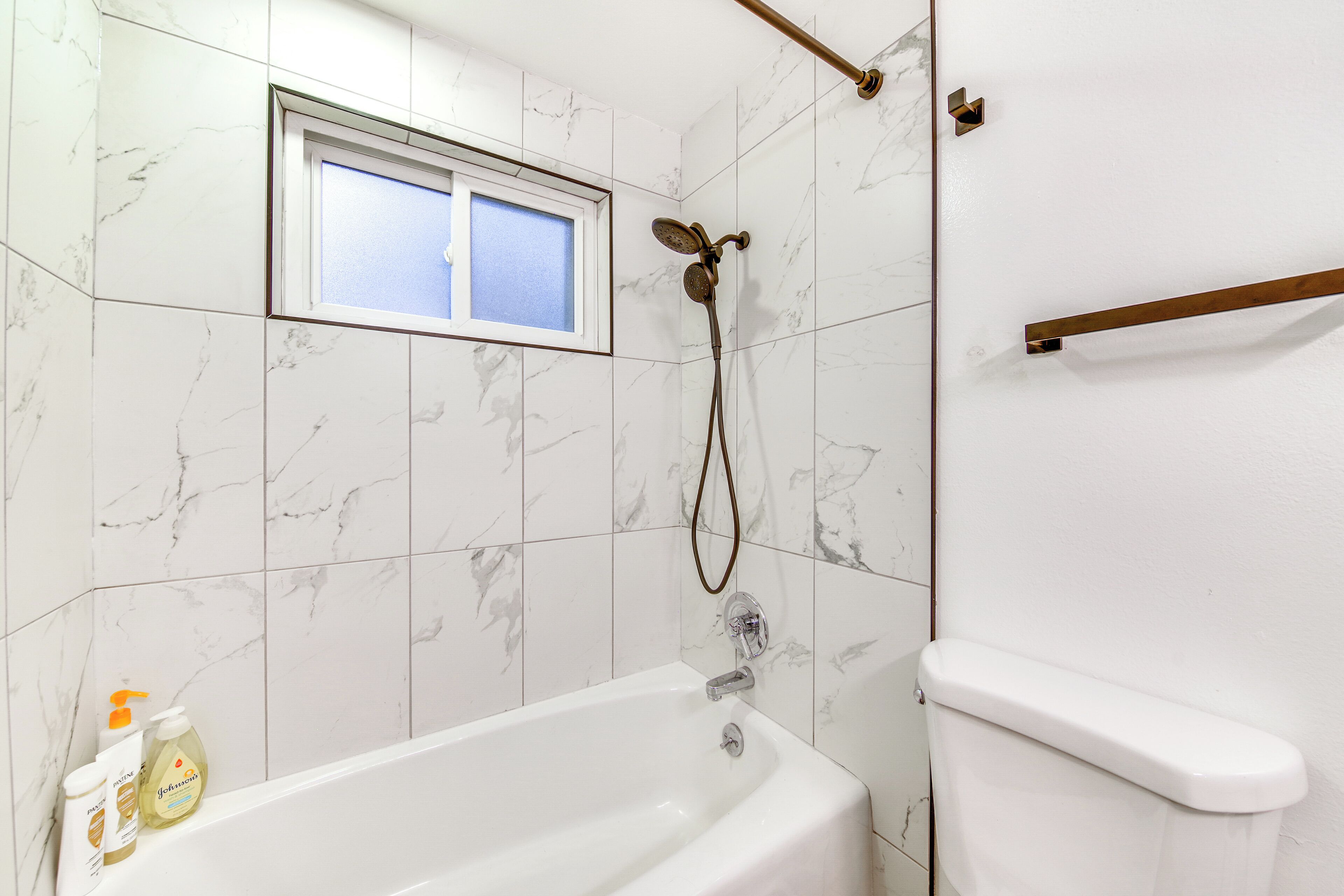A bathroom with a bathtub, a shower, and a toilet. There is a window above the bathtub and a towel rack on the wall.