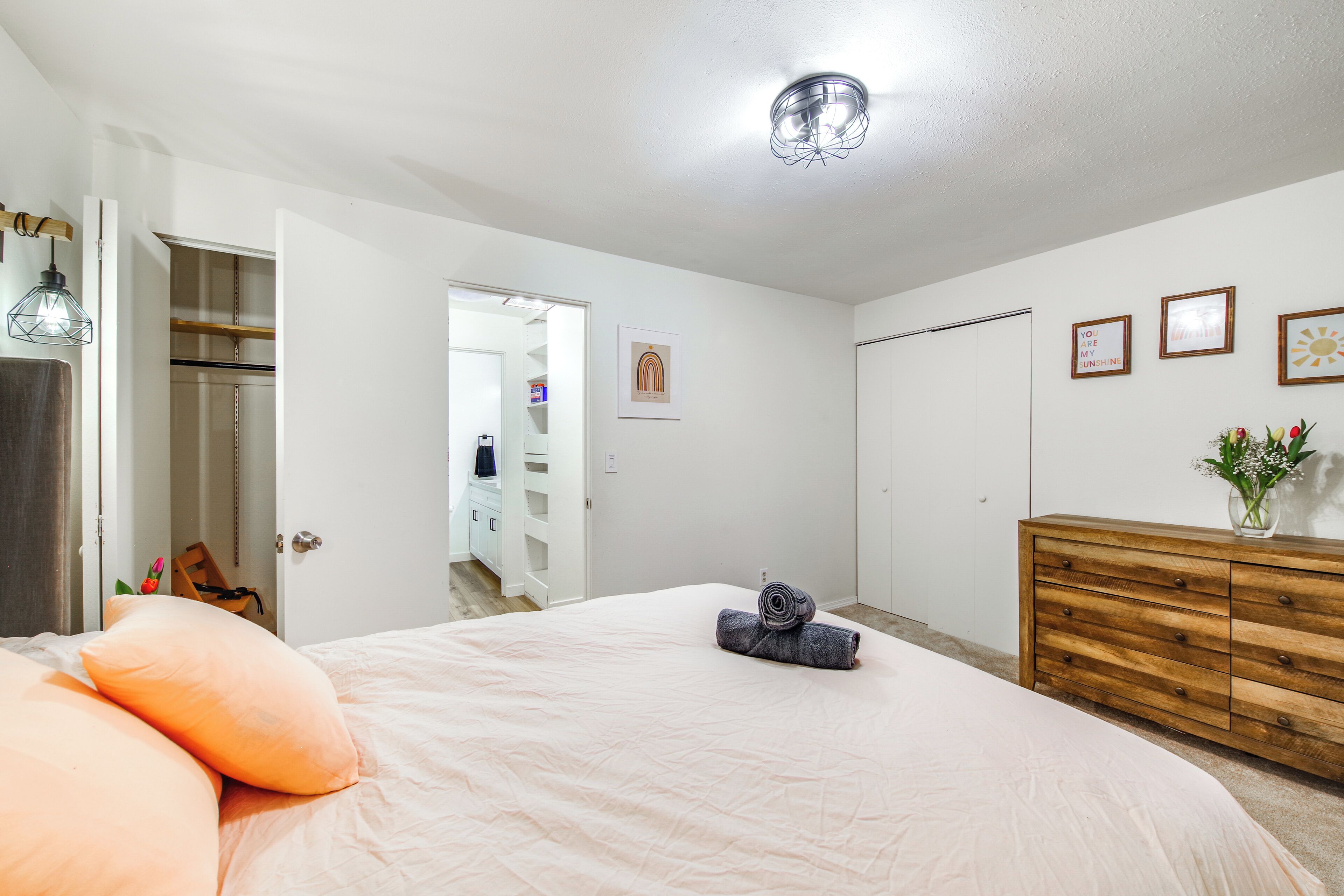 A bedroom with a bed, a wooden dresser, a closet, and a bathroom visible through an open door.