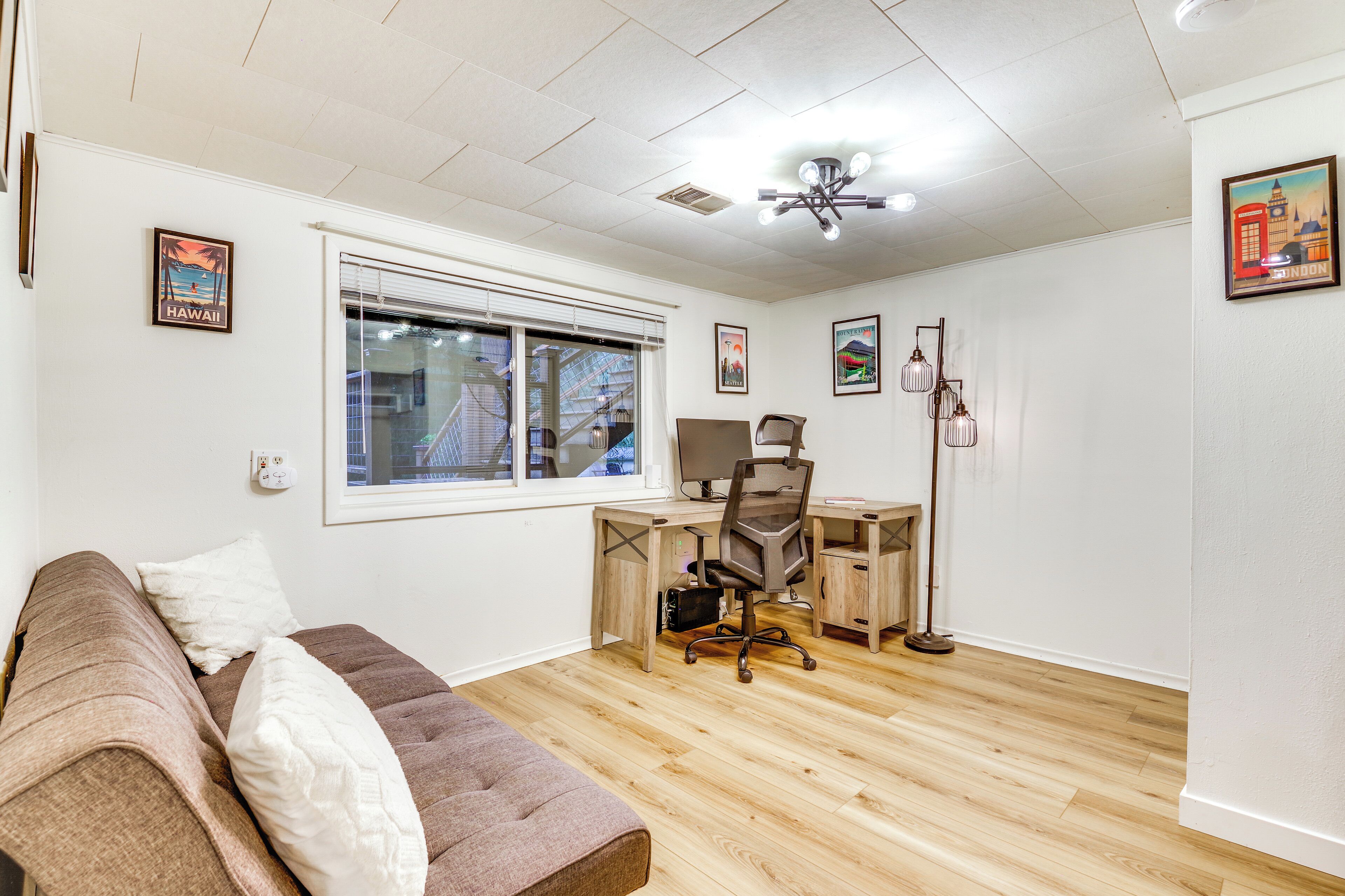 A room with a wooden floor, a desk with a computer, a chair, a couch, and a window.