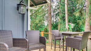 A covered outdoor deck with wicker furniture and a table, surrounded by trees. - Classic Woodinville Wine Country Escape! (Woodinville)