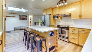 A modern kitchen with wooden cabinets, a central island with stools, stainless steel appliances, and a skylight. - Classic Woodinville Wine Country Escape! (Woodinville)