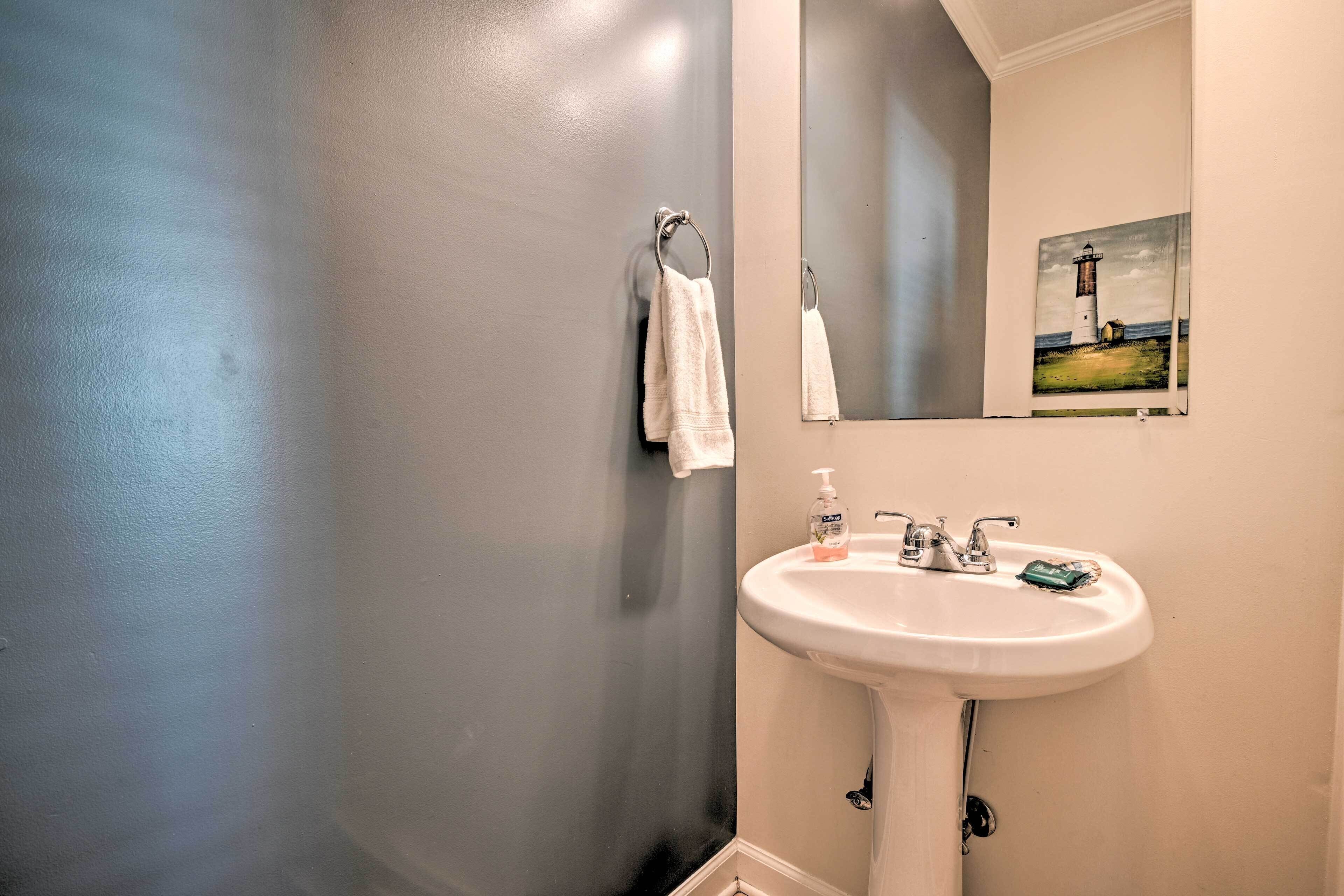 A bathroom with a white sink, a mirror, and a painting of a lighthouse.