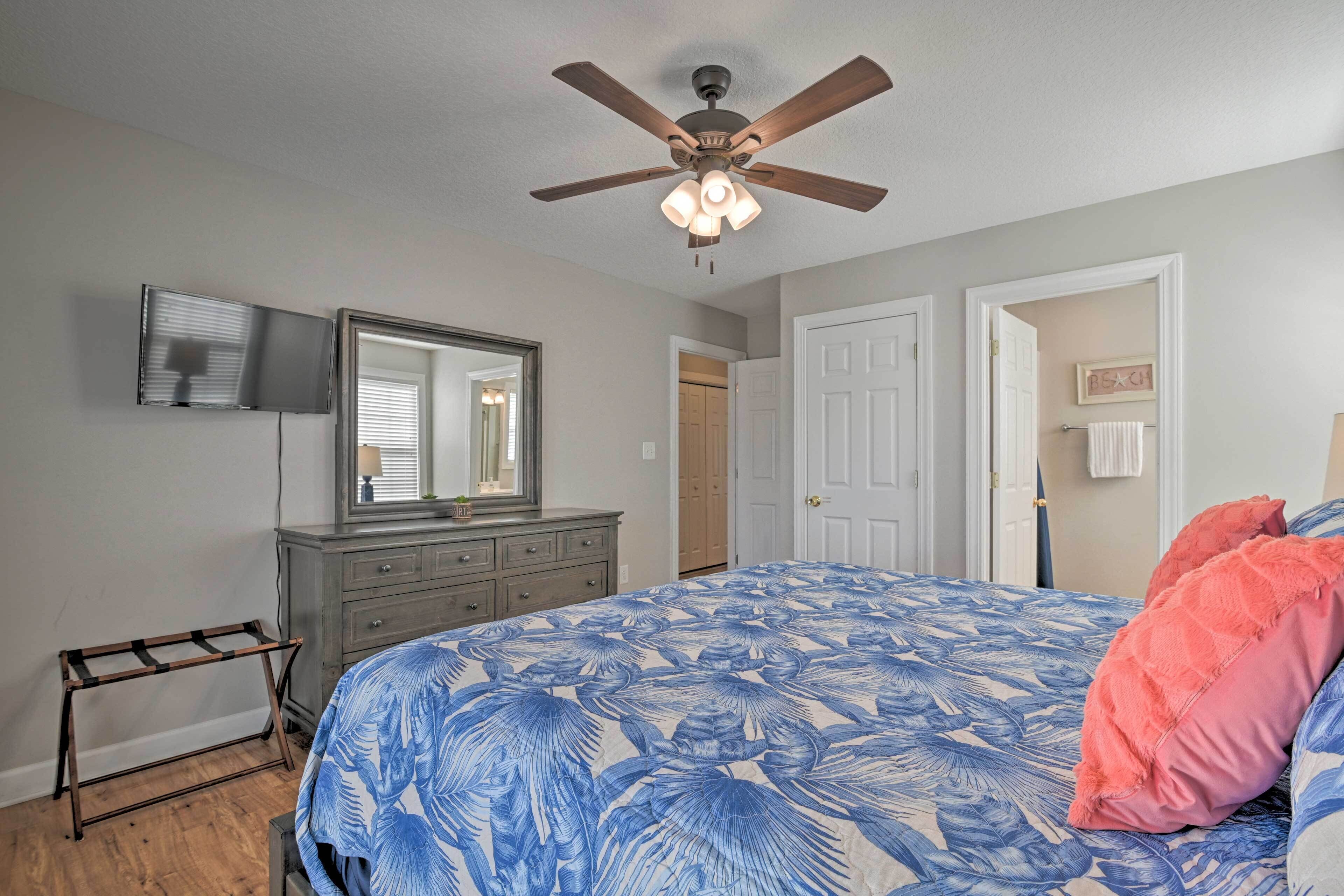A bedroom with a bed, a ceiling fan, a dresser, a mirror, and a door.
