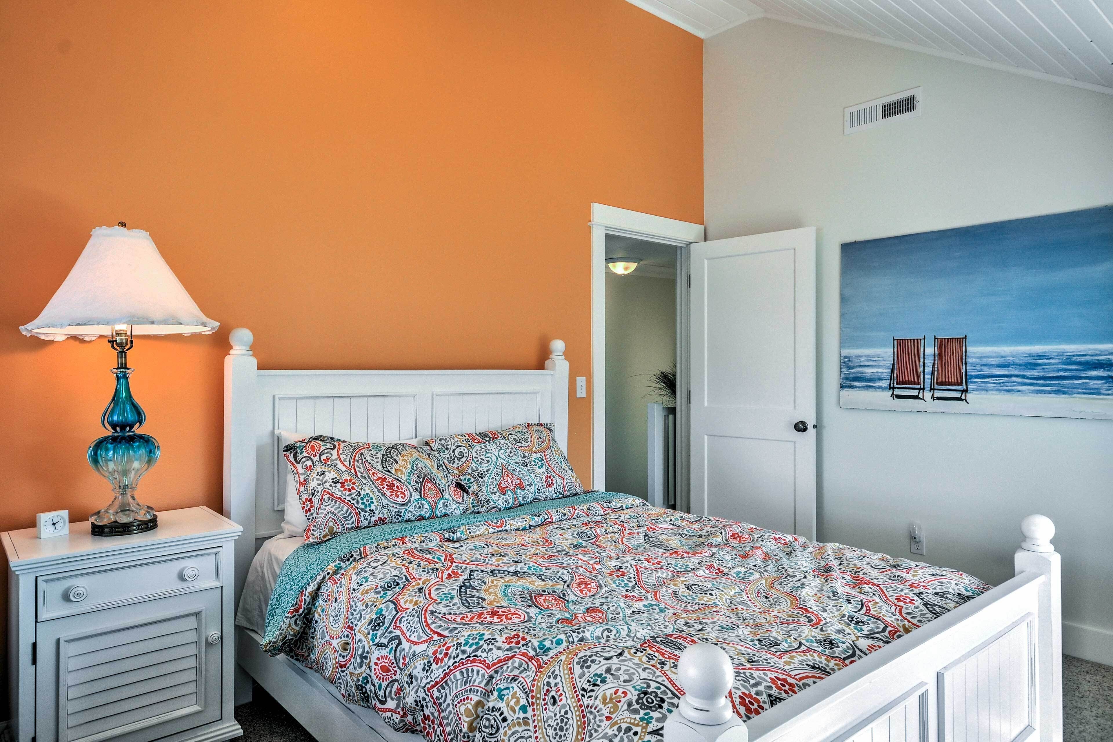 A bedroom with a patterned bedspread, a bedside lamp, and a painting of a beach scene on the wall.