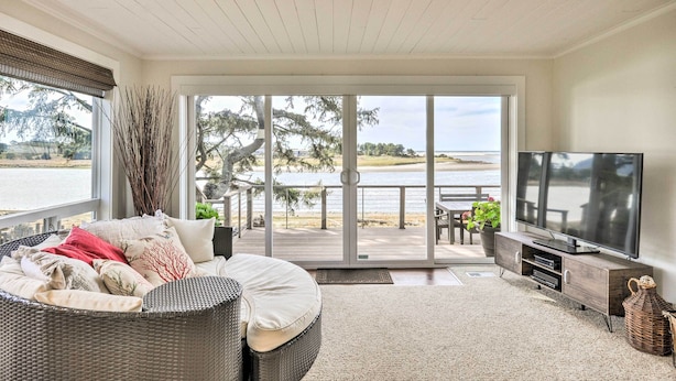 Una sala de estar con televisor grande, muebles de mimbre y una puerta corrediza de vidrio que da a una terraza con vista a un lago.