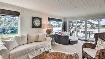 A living room with a beige sofa, a round wicker chair, a cowhide rug, and a large window with a view of trees and a building.