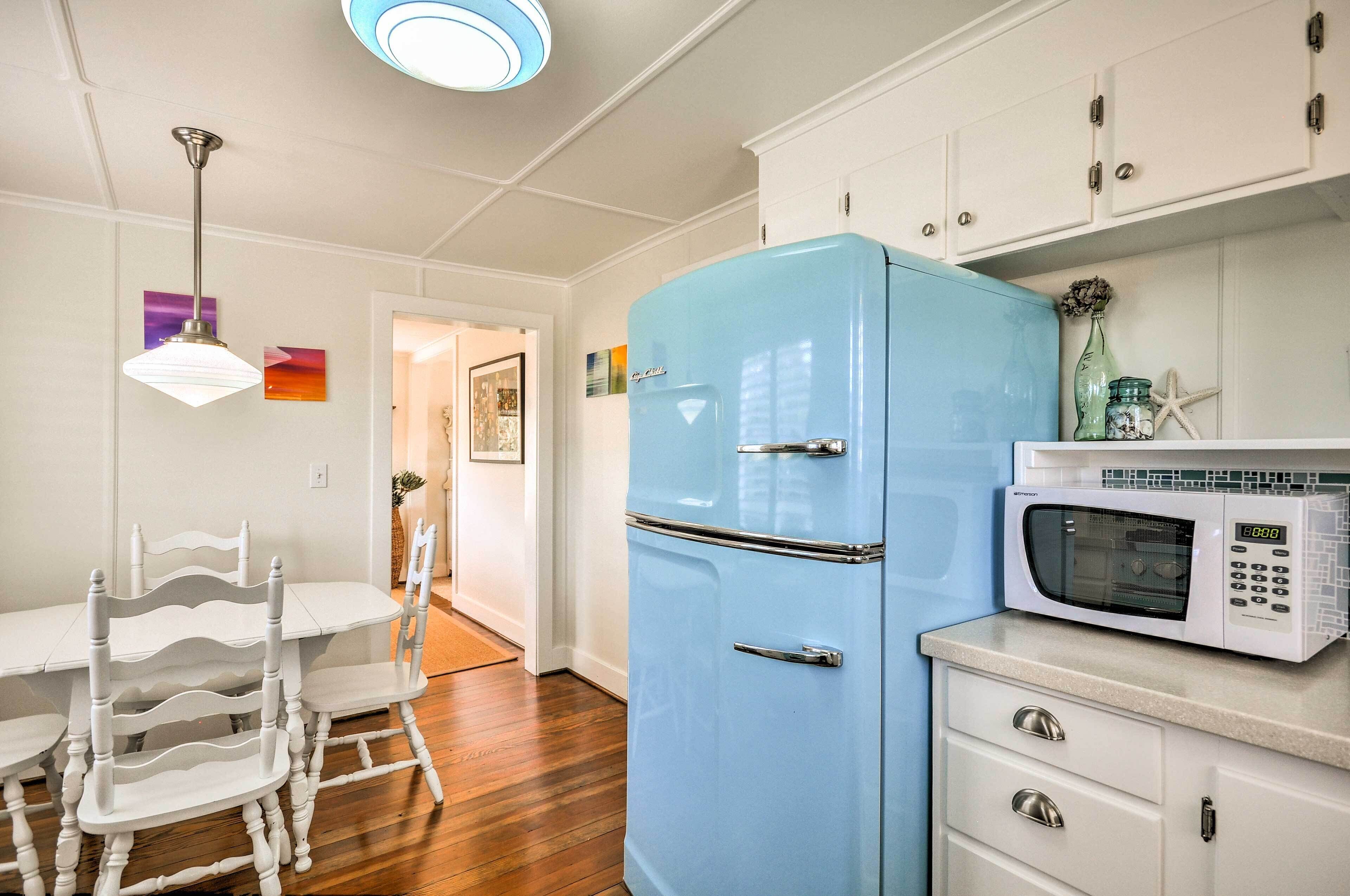 A kitchen with a blue refrigerator, a white microwave, and a dining area with white chairs and a table.