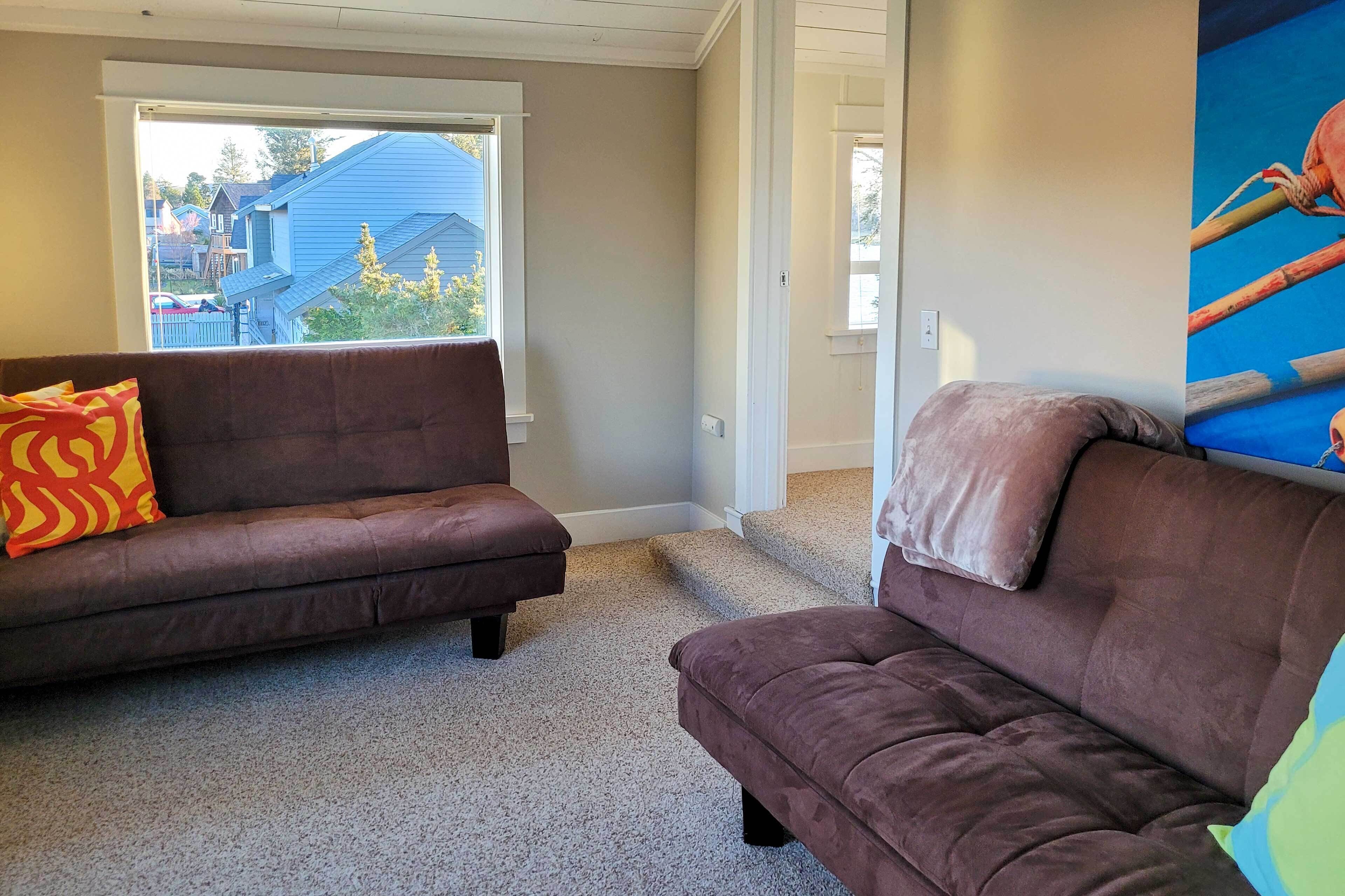 A room with two brown sofas, a large window, and a view of houses outside.