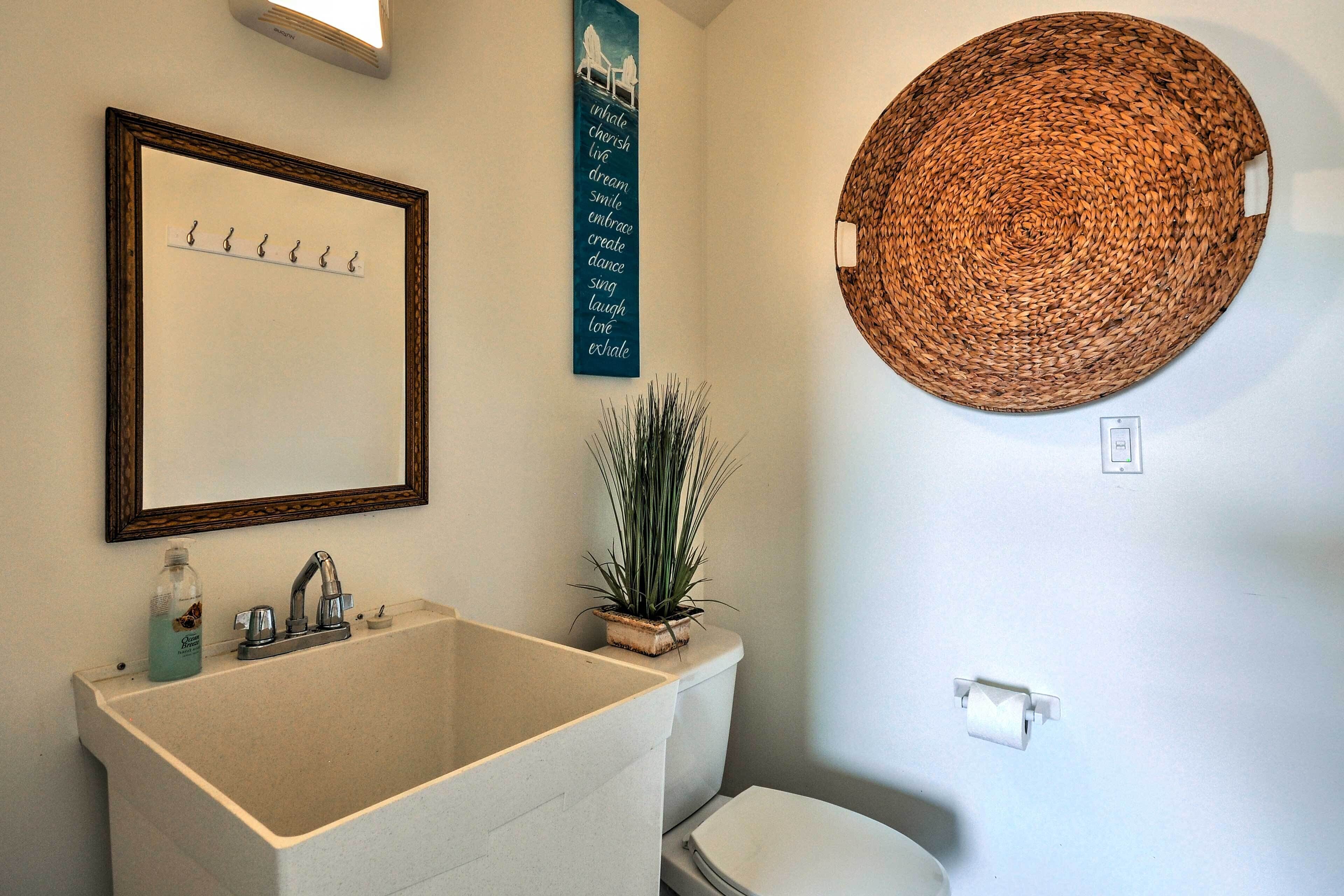 A bathroom with a large sink, a mirror, a wall-mounted toilet paper holder, and a woven basket on the wall.