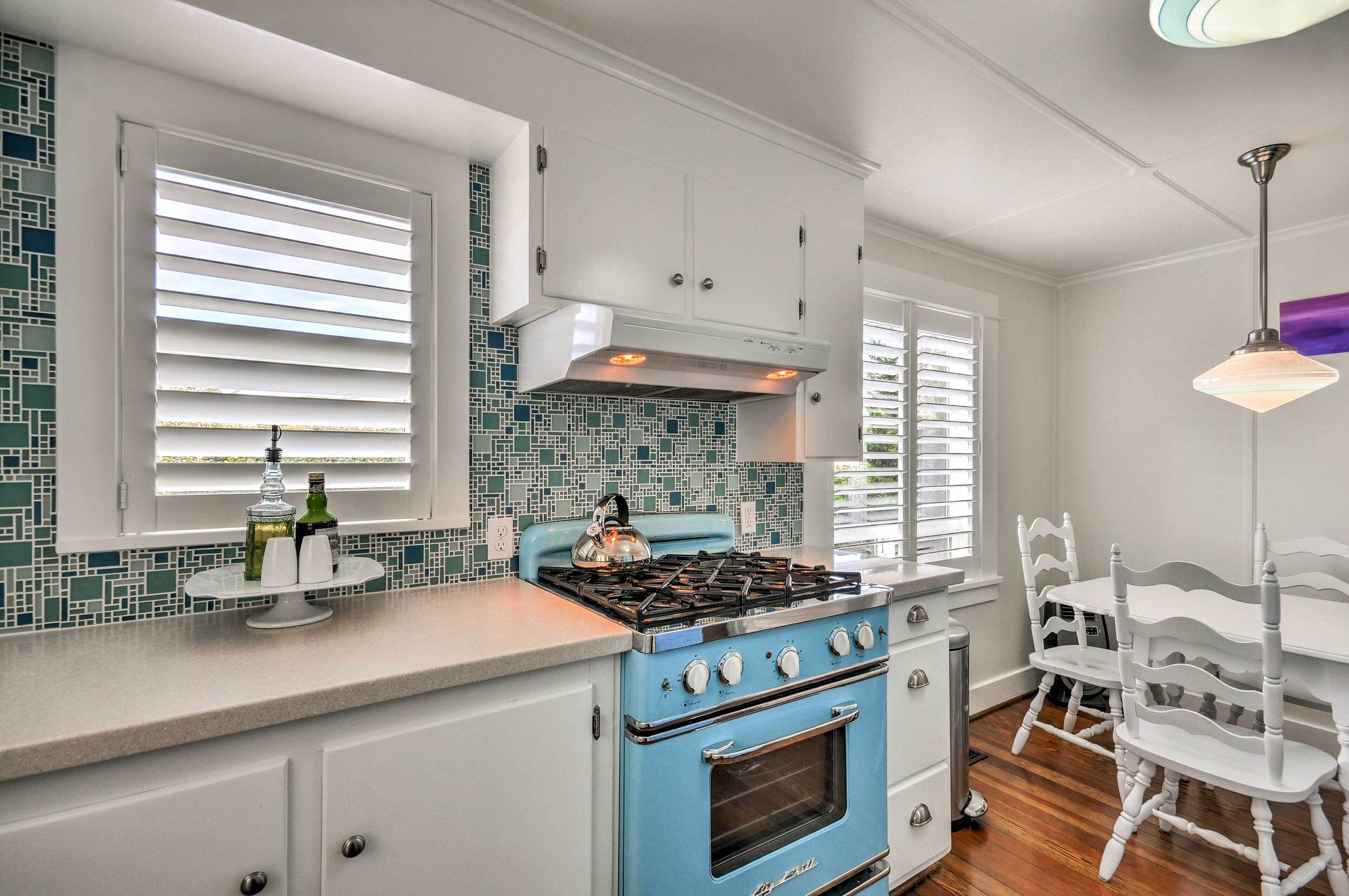 Una cocina con estufa azul, armarios blancos y salpicadero de azulejos.