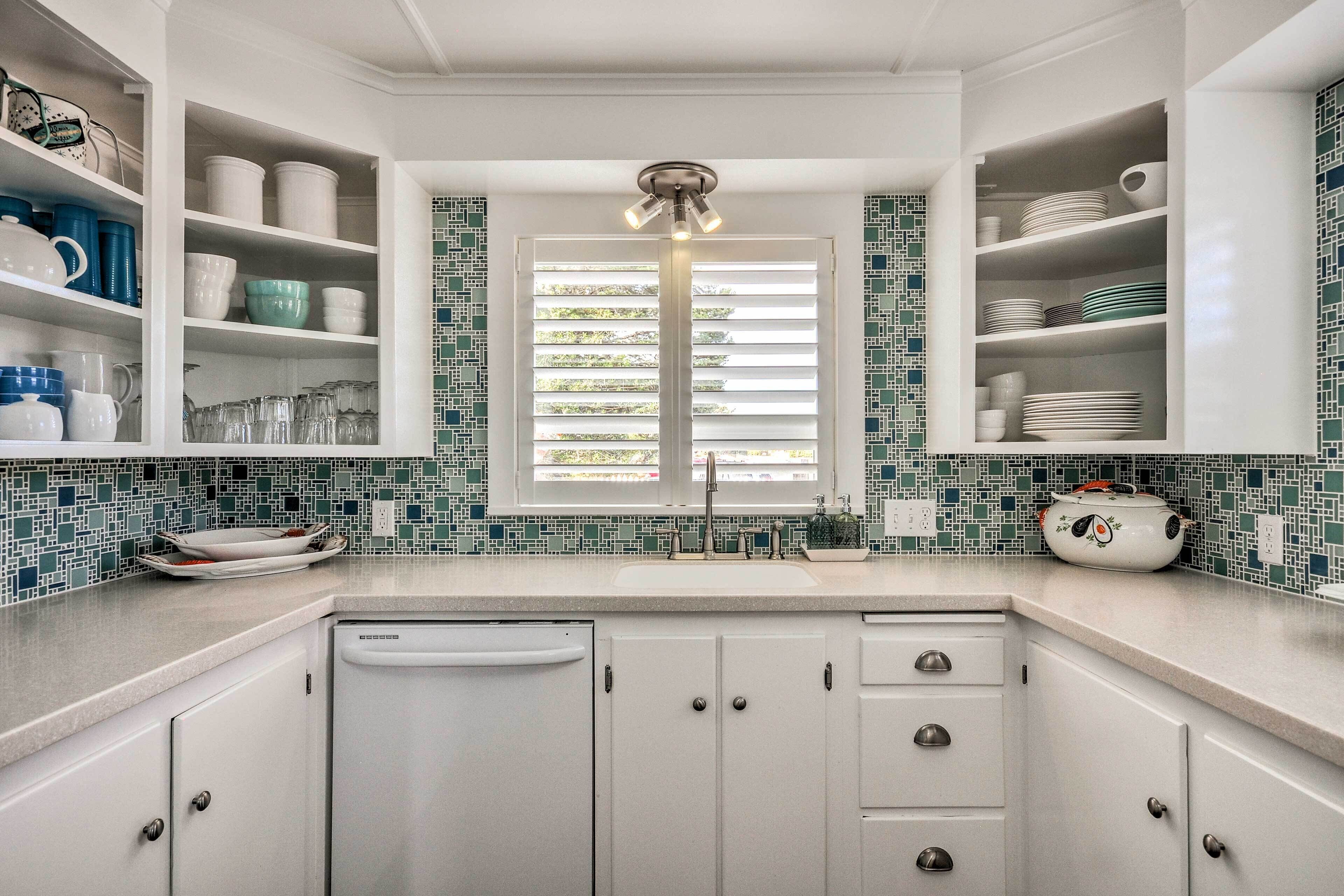 A kitchen with white cabinets, a dishwasher, and a window with blinds.