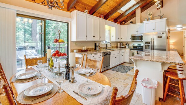 A spacious kitchen with white cabinets, a large island, and a dining area with a wooden table set for six. - Spacious House w/ Deck & Grill in South Lake Tahoe (South Lake Tahoe)