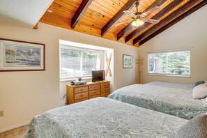A bedroom with two beds, wooden ceiling beams, a ceiling fan, and two windows with blinds.