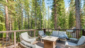 A deck with wicker furniture and a table, surrounded by tall pine trees. - Spacious House w/ Deck & Grill in South Lake Tahoe (South Lake Tahoe)