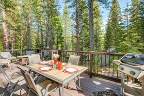A deck with a table set for dining, surrounded by chairs, and a grill.