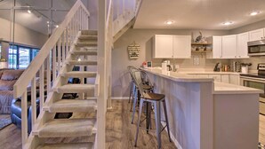 A modern kitchen with white cabinets, a central island with stools, and a staircase leading to another level. - 2 Mi to Margaritaville! Lake-view Retreat w/ Pool (Osage Beach)