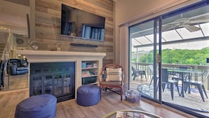 A modern living room with a fireplace, a television mounted on a wooden wall, and a large sliding glass door leading to an outdoor patio area. - 2 Mi to Margaritaville! Lake-view Retreat w/ Pool (Osage Beach)