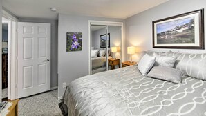 A bedroom with a large bed, a door, a mirror, a nightstand, and a framed picture on the wall. - Charming Historic Condo - Walk to Downtown & UW (Laramie)