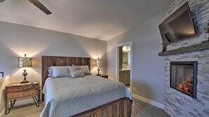 Ein Schlafzimmer mit Bett, Nachttischen, Fernseher, Kamin aus Stein und Deckenventilator.