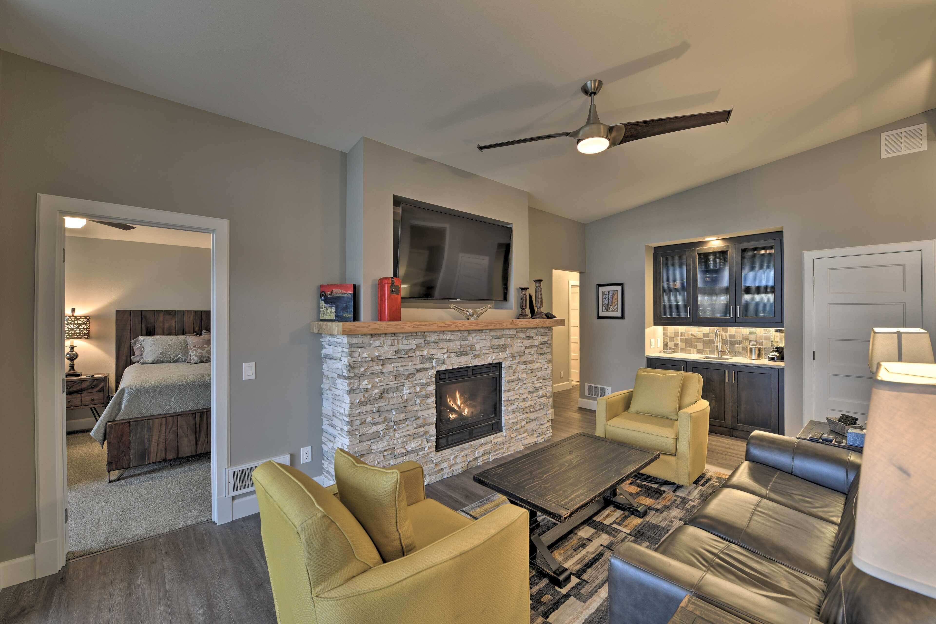 A modern living room with a stone fireplace, a flat-screen TV, and a ceiling fan.