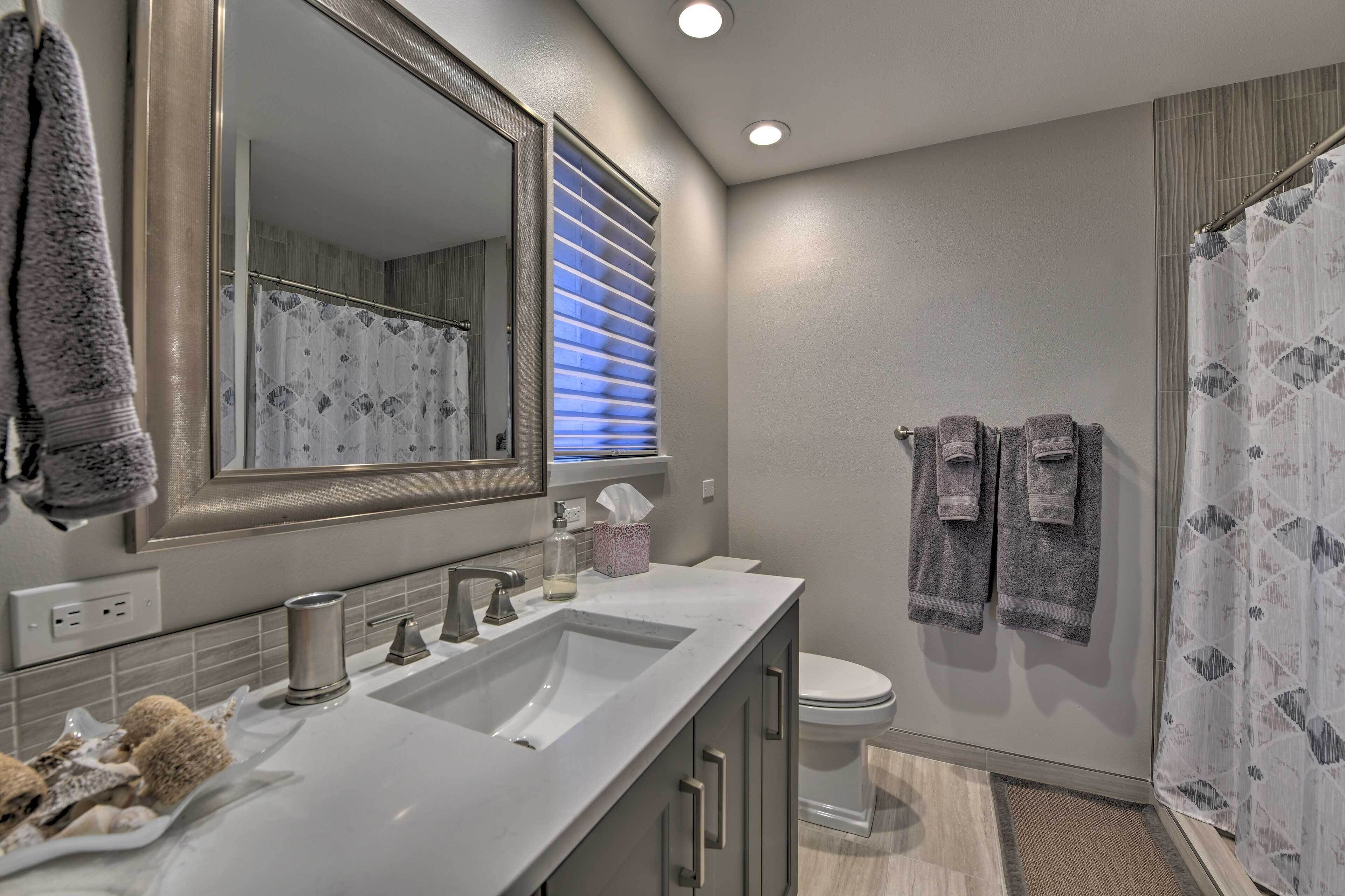 A modern bathroom with a large mirror, two sinks, a toilet, and a shower area.