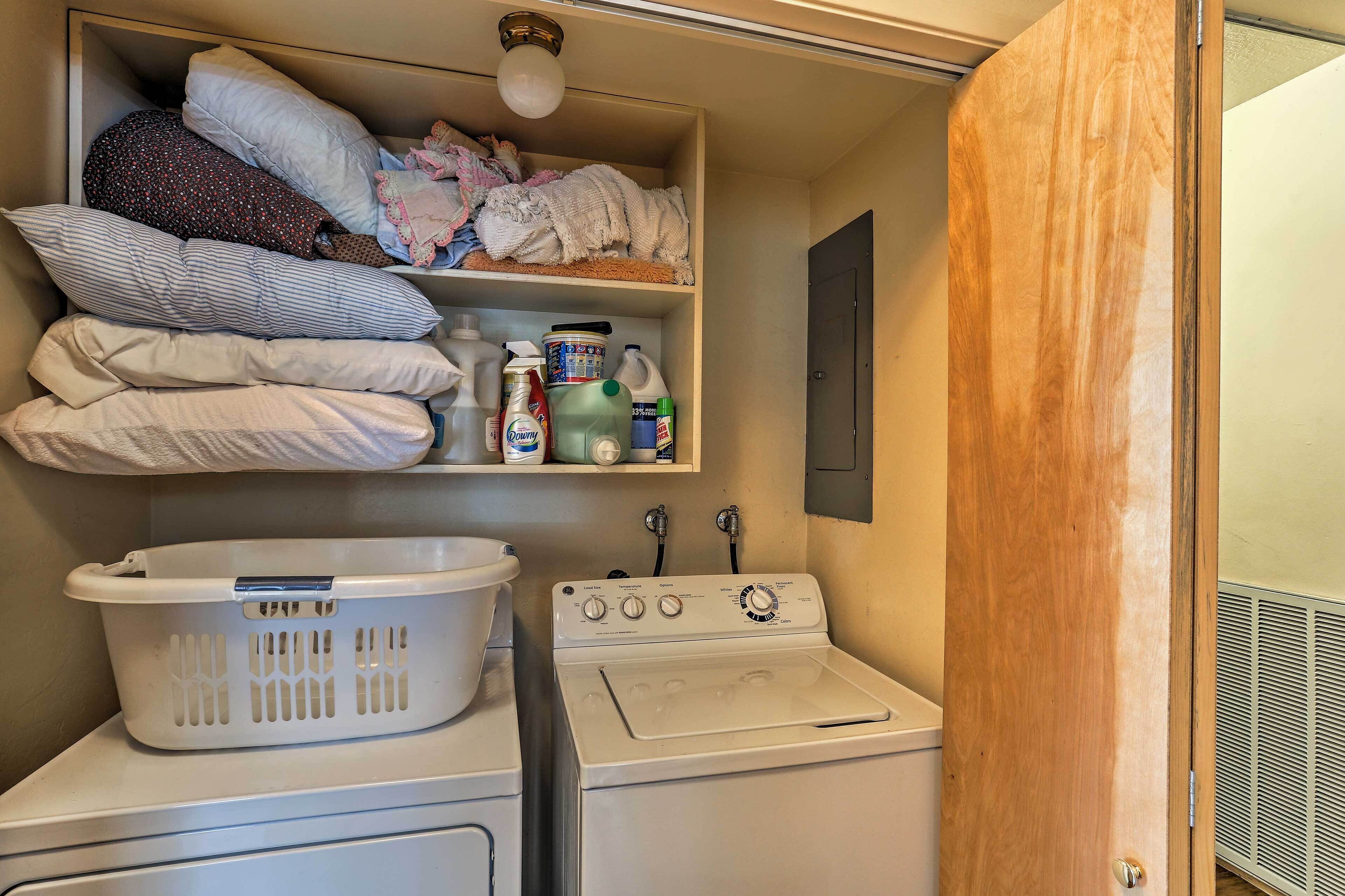 A laundry area with a washing machine, a dryer, a shelf with pillows and laundry supplies.