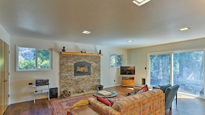 A spacious living room with a stone fireplace, a large window, and a cozy seating area. - Lake Almanor Country Club Home w/ Views! (Westwood)