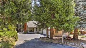A residential property with a paved driveway leading to a house surrounded by tall evergreen trees. - Lake Almanor Country Club Home w/ Views! (Westwood)