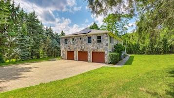A two-story stone house with a paved driveway and a well-maintained lawn.