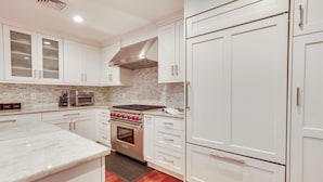 Una cocina con armarios blancos, una campana extractora de acero inoxidable y un horno empotrado.