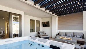 Ein moderner Außenbereich mit Whirlpool, Sitzgelegenheiten und einer Pergola mit Lichterketten.