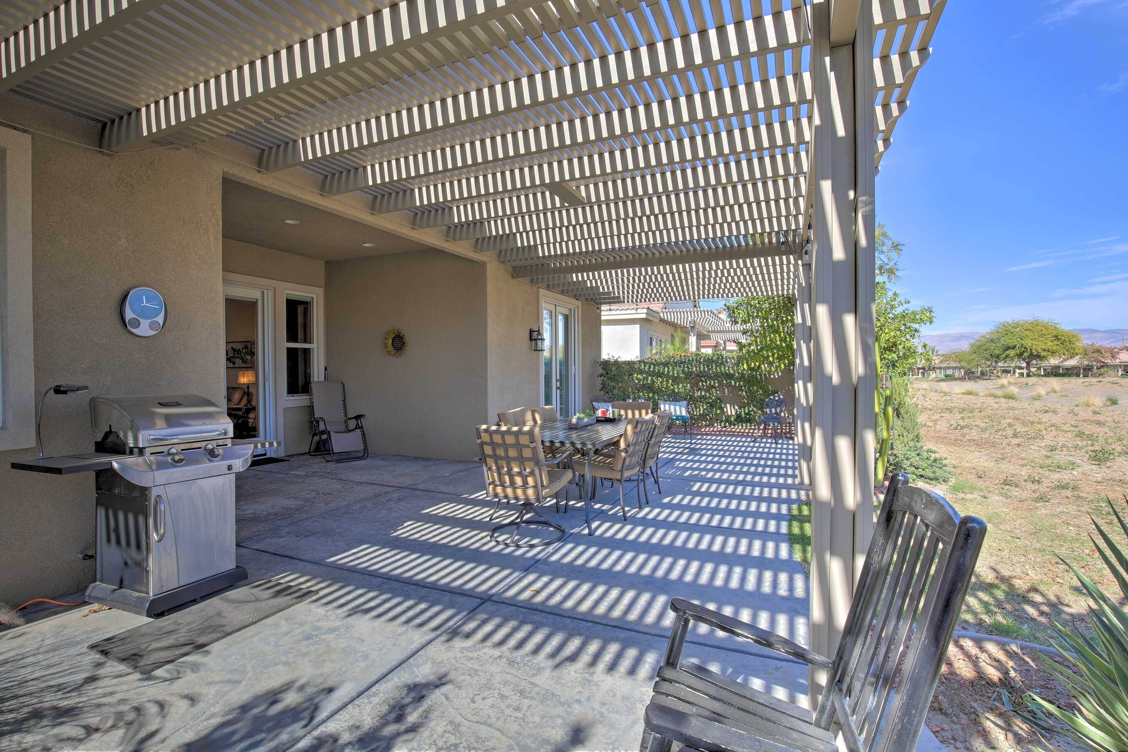 An outdoor patio with a grill, dining table, and chairs.