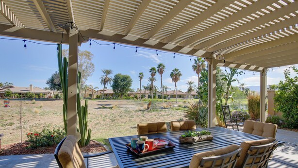 A covered patio with a table set for two, surrounded by cushioned chairs. - 1 Mi to Coachella: Serene Retreat w/ Pool Access (Indio)