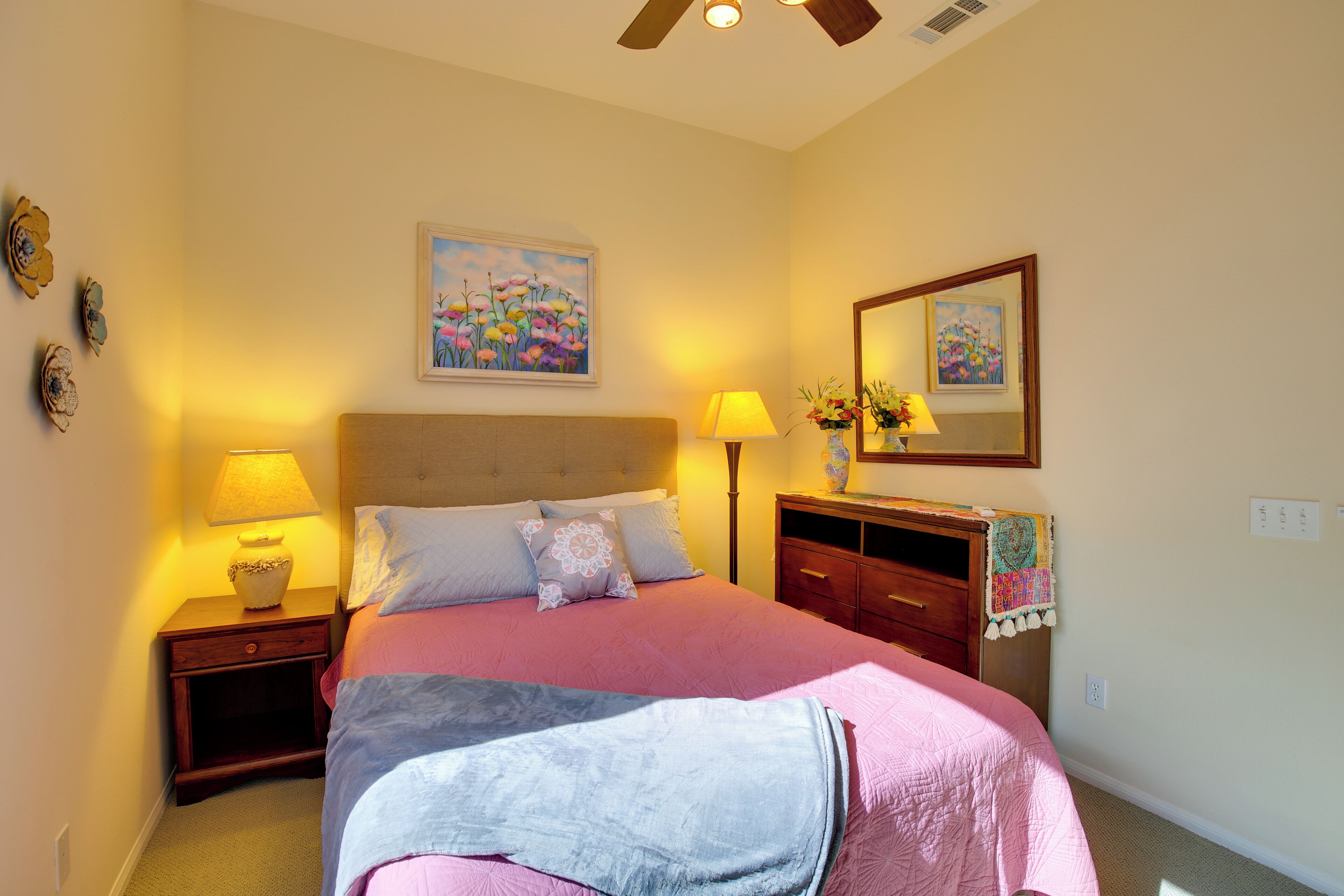 A bedroom with a bed, two bedside tables, a nightstand, a dresser, a ceiling fan, and two wall-mounted lamps.