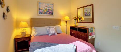 A bedroom with a bed, two bedside tables, a nightstand, a dresser, a ceiling fan, and two wall-mounted lamps.