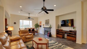 A spacious living room with a leather sofa, a wooden coffee table, and a fireplace. There is a ceiling fan, a TV, and a dining area with chairs. - 1 Mi to Coachella: Serene Retreat w/ Pool Access (Indio)