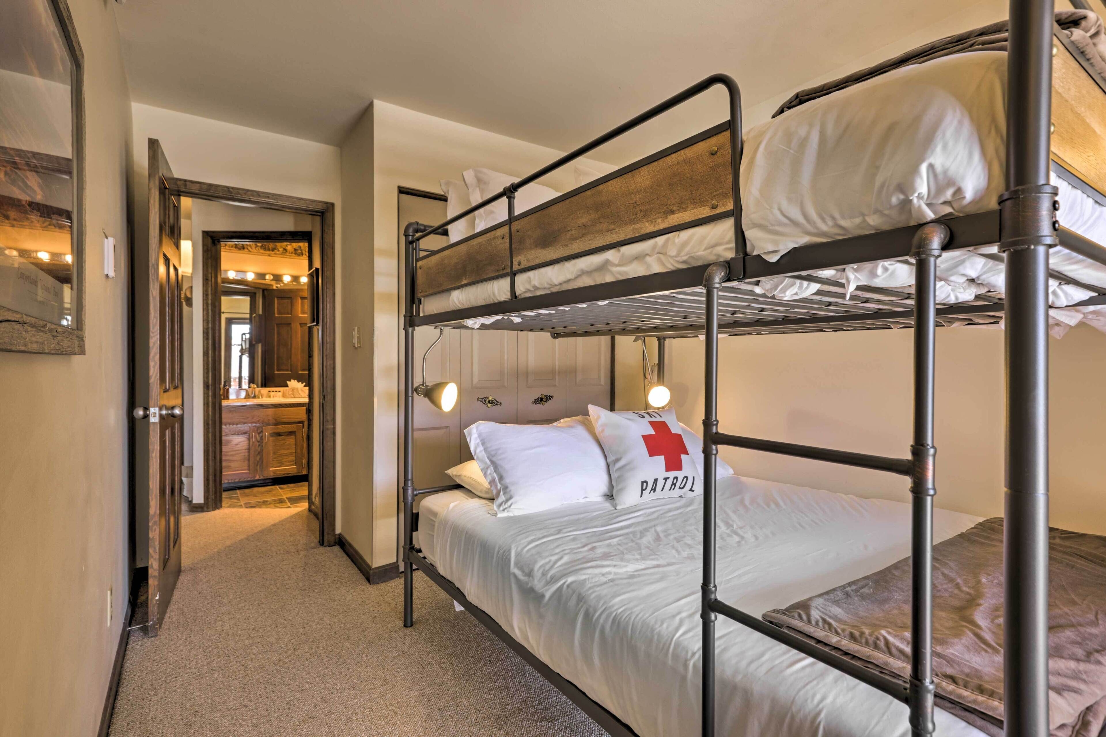 Habitación con literas, cabecero de madera, ropa de cama blanca y almohada con una cruz roja.