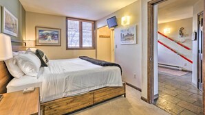 Ein Schlafzimmer mit einem hölzernen Bett, einem Nachttisch, einem Fenster mit Jalousien, einem an der Wand montierten Fernseher und Wandleuchten.