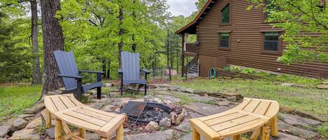 A cabin with a stone fire pit and two Adirondack chairs in a wooded area.
